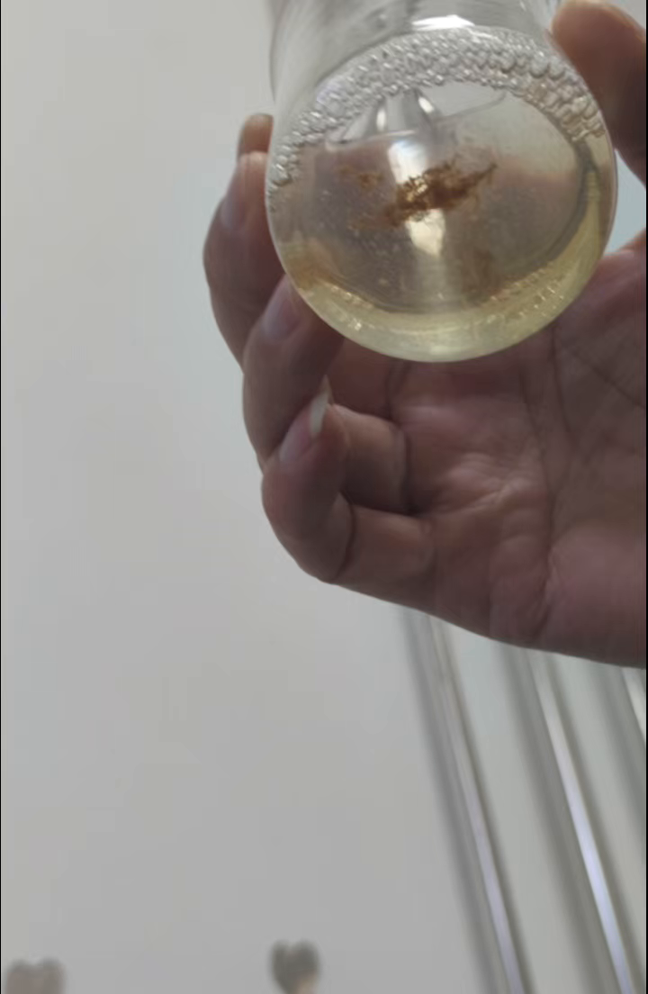 Actual factory video frame at 48 seconds showing the cup and dark-brown post-rinse flocculent aggregates